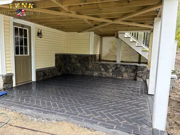 Herringbone paver patio under an elevated deck with stone knee wall