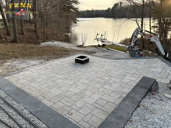 Paver patio taking shape at the lake with an excavator on site