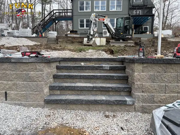 Block retaining wall with built-in stone steps behind the home