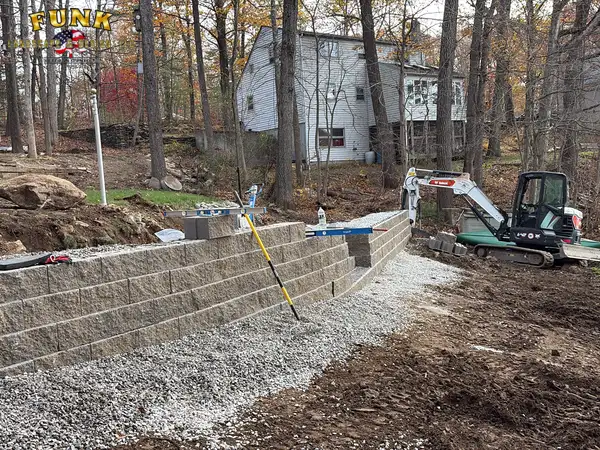 Mini excavator assisting retaining wall construction on a slope