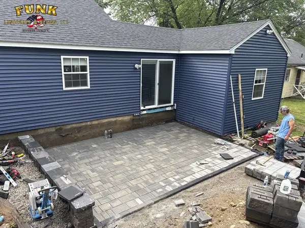 Paver patio being installed behind a blue home with block staged