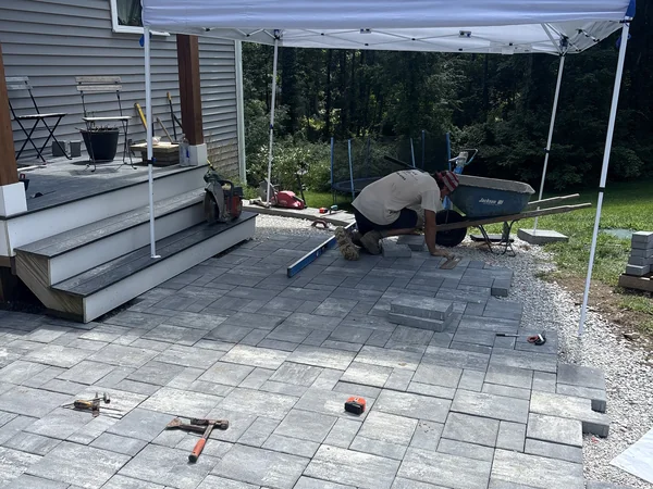 Crew member leveling paver blocks on a new patio installation, with level and rubber mallet, by Funk Landscape & Design