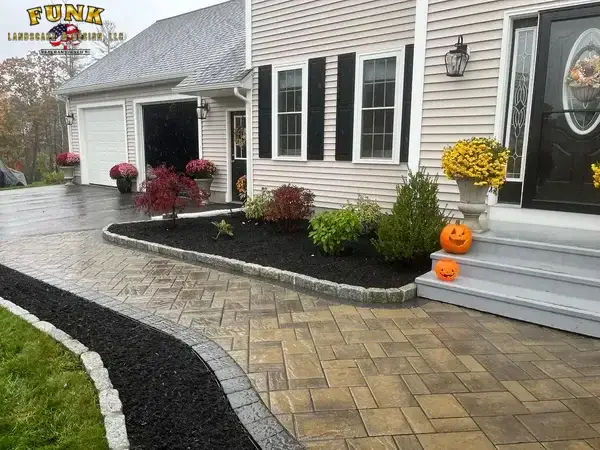 Fresh mulch beds with cobblestone edging beside a paver walkway and front steps by Funk Landscape & Design