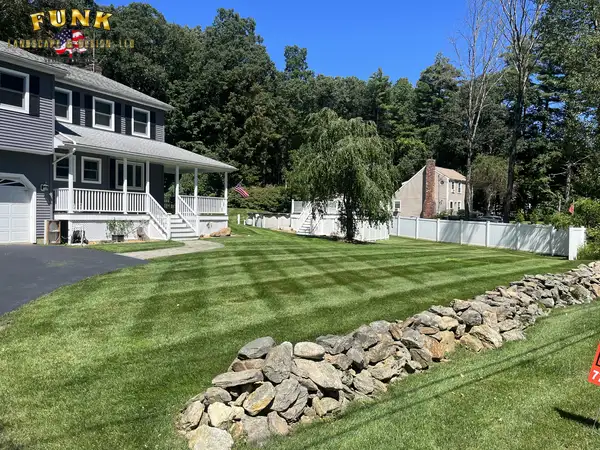Freshly striped front lawn wrapping around a natural stone wall