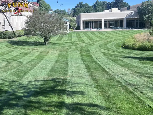 Freshly striped commercial lawn beside a brick building, maintained by Funk Landscape & Design